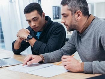 behaviour support practitioner receiving supervision and guidance from a senior professional in a collaborative office setting with training materials