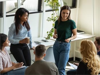 Group of people in a training session, with one person presenting and others seated and listening in a bright office setting, symbolising professional development and collaborative learning.